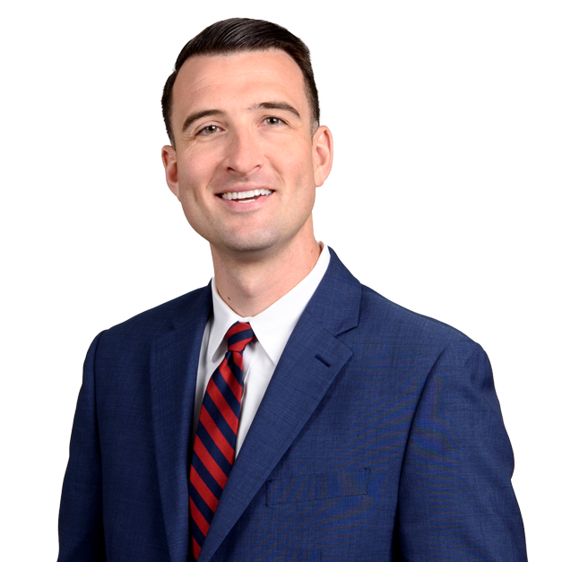 Man in a blue suit and red striped tie smiling, standing in front of a blurred light-colored background.