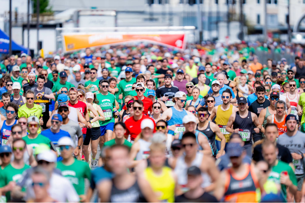 A large crowd of runners in athletic gear participates in an outdoor race event on a city street.